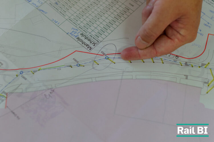 A hand points to a marked-up site plan showing manhole locations and inspection details.